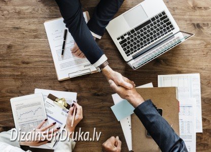 vizitkartes_dizains_2019-1 Business partners shaking hands over a table with laptop and documents, discussing business cards