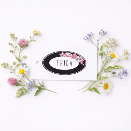 Custom hang tag with floral design and FRIDA text among meadow flowers