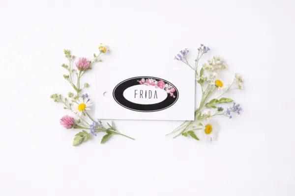 Kartona birka ar ziedu dizainu un tekstu FRIDA starp pļavas ziediem