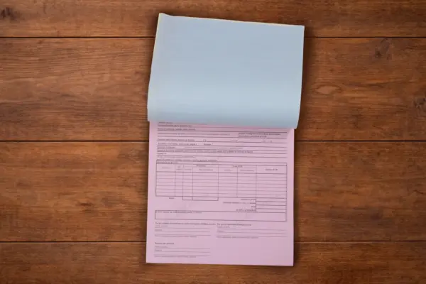 Paškopējošo veidlapu bloks ar atšķirtu zilu lapu un rozā kopiju uz koka fona