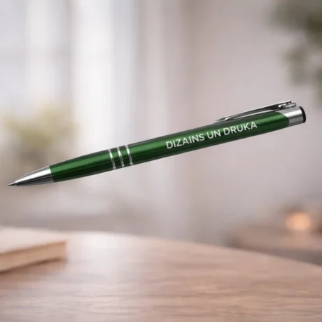 Green engraved metal pen with white text on a blurred interior background