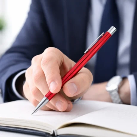 Hand holding a red metal pen over an open notebook