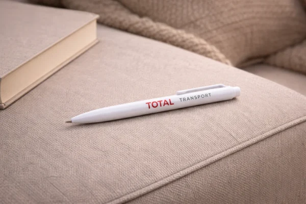 Белая пластиковая ручка с принтом TOTAL TRANSPORT на бежевой тканевой поверхности