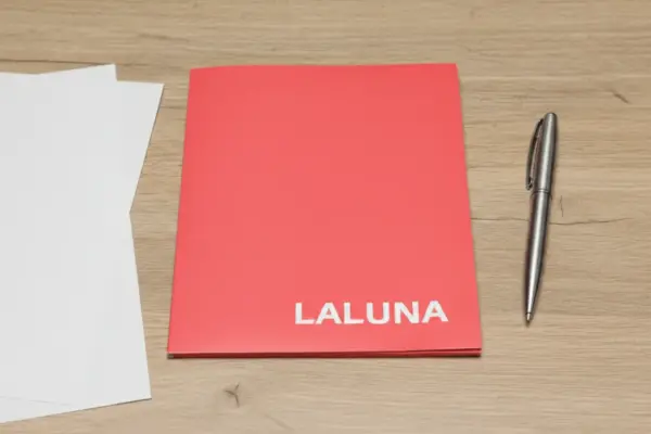 Red custom document folder with white LALUNA print on a wooden desk beside a pen