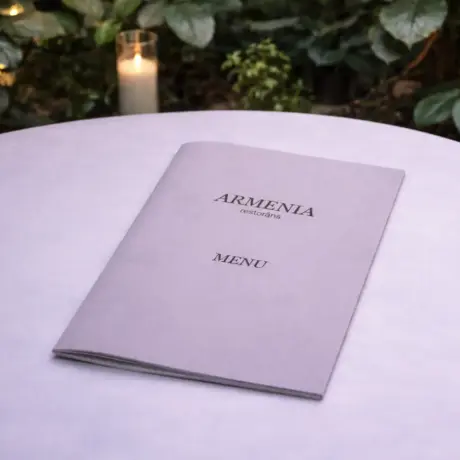 Eleganta daudzlapu ēdienkarte restorānam Armenia uz balta galda ar sveci fonā