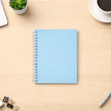 Gaiši zils spirāļu bloknots uz koka galda ar biroja piederumiem