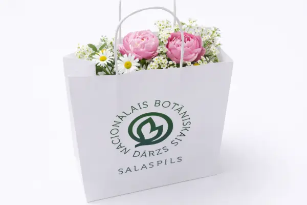Balts papīra maisiņš ar apdruku Nacionālais botāniskais dārzs, pildīts ar ziediem