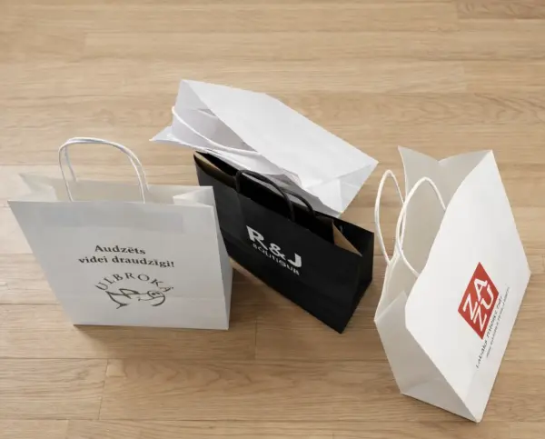 Balti un melni papīra maisiņi ar apdruku un logo uz koka grīdas