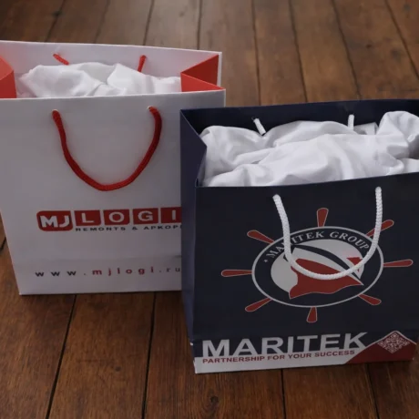 Divi dāvanu maisiņi ar apdruku un auklas rokturiem uz koka grīdas