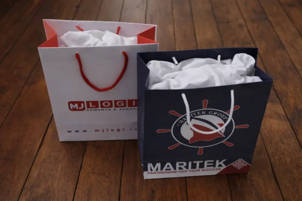 Divi dāvanu maisiņi ar apdruku un auklas rokturiem uz koka grīdas