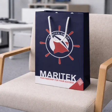 Tumši zils dāvanu maisiņš ar apdruku un auklas rokturiem uz krēsla