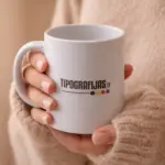 Balta keramikas krūze ar apdruku Tipografijas.lv rokās