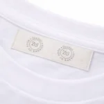 Kokvilnas birka ar druku iešūta balta T-krekla apkaklē