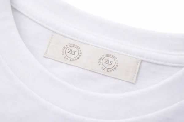 Kokvilnas birka ar druku iešūta balta T-krekla apkaklē