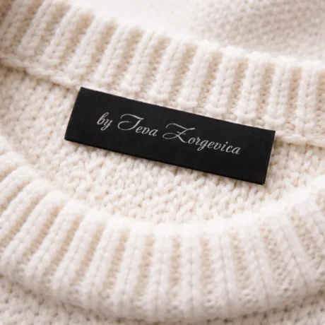 Black custom woven jacquard label with white text on the collar of a white knitted sweater