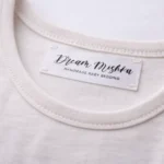 Gaišā apģērbā iešūta satīna birka ar melnu Dream Mishka druku