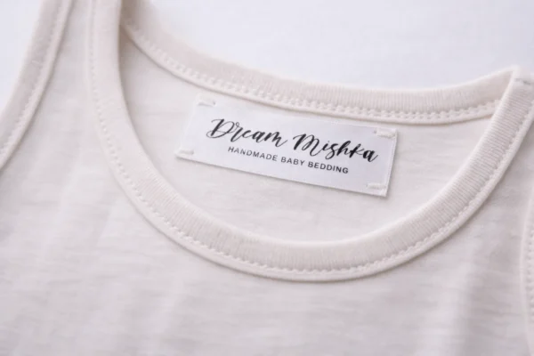 Gaišā apģērbā iešūta satīna birka ar melnu Dream Mishka druku